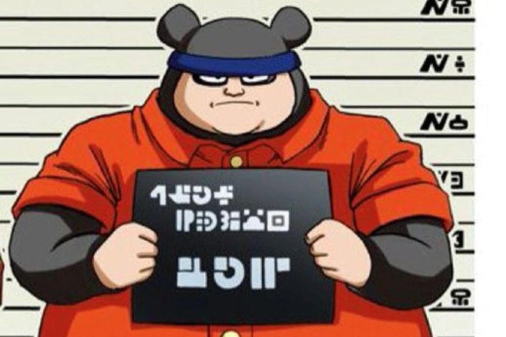 Personnage trapu portant une tenue orange de prisonnier, avec un bandeau bleu et un panneau d’identification, posé devant un fond de prise de vue policière.